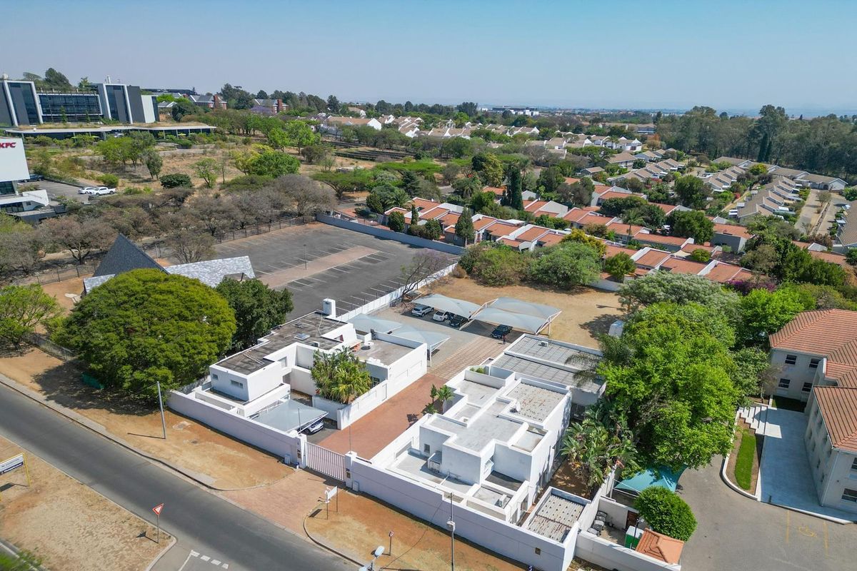 Aerial view of a commercial property complex featuring multiple white buildings, paved parking areas, and shaded carports within a landscaped suburban setting.