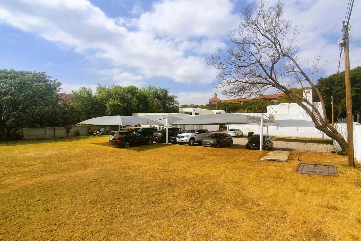 Outdoor parking area featuring shade cloth structures for vehicle protection, set within a large open grassed lot.