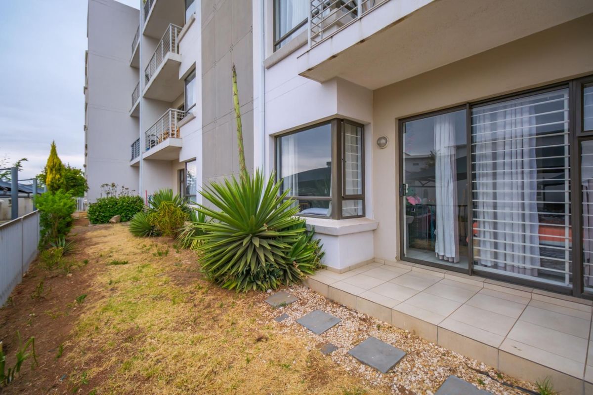 Ground floor apartment exterior featuring a tiled patio area, sliding glass doors with security bars, and a small private garden space.