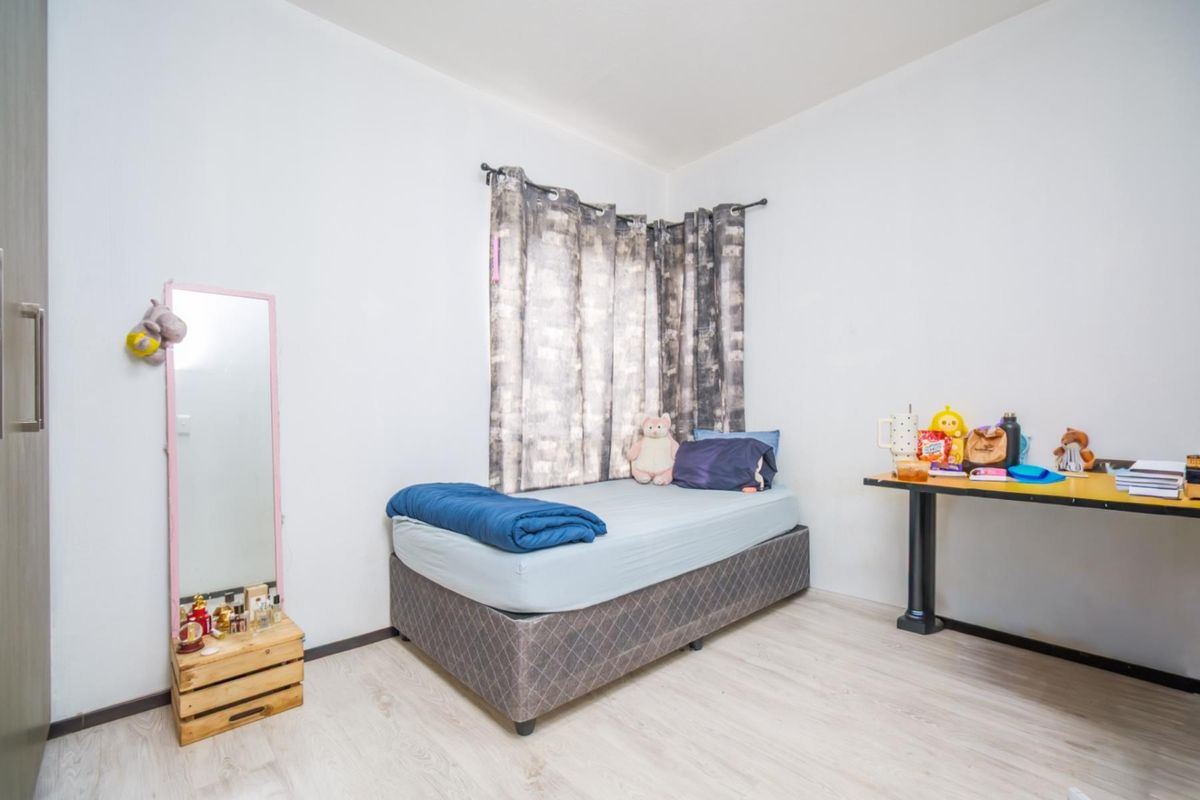 A functional bedroom featuring light-toned laminate flooring and a window with curtain tracks.