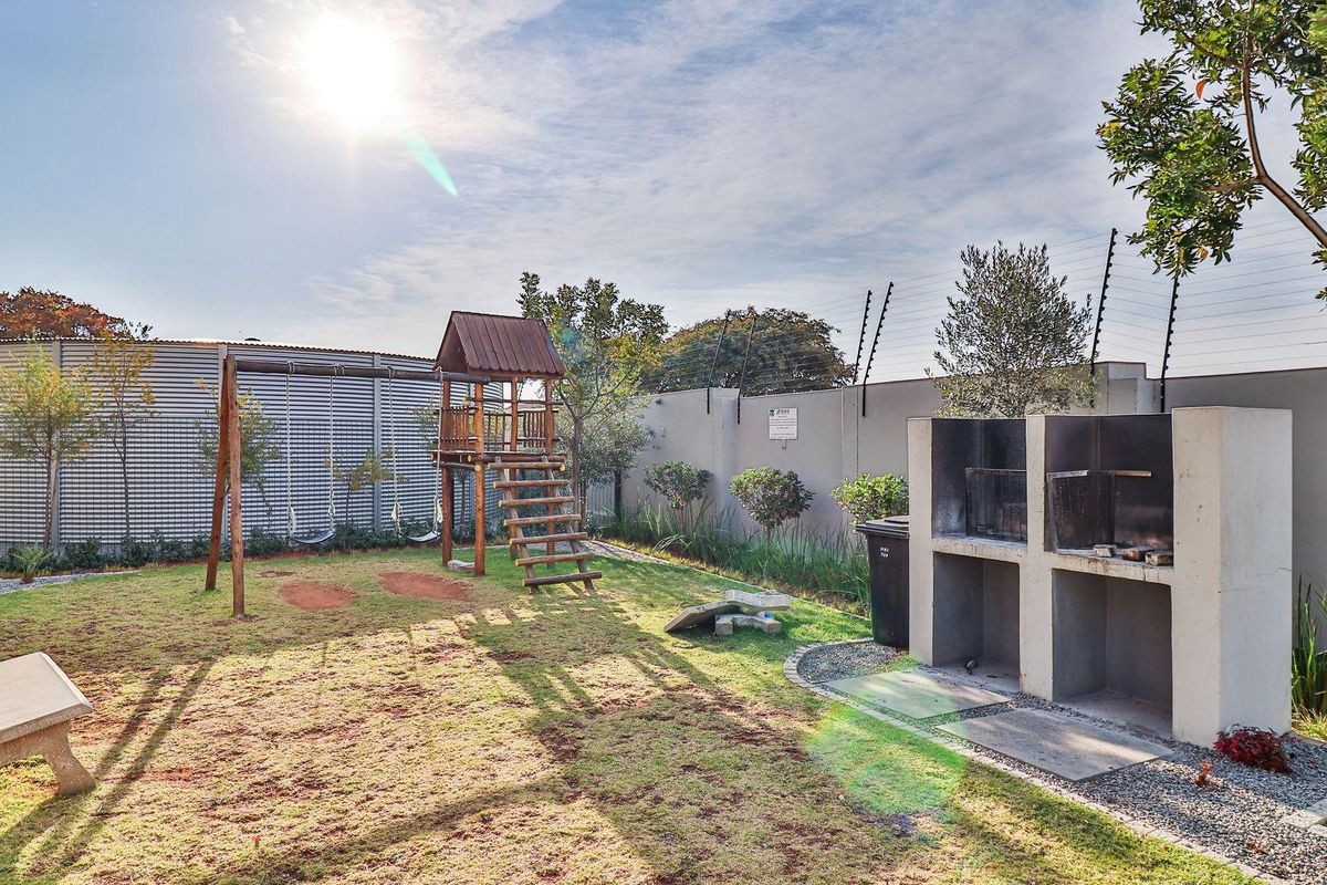 A private rear garden featuring a built-in concrete braai area, lawn space, and perimeter wall with electric fencing.