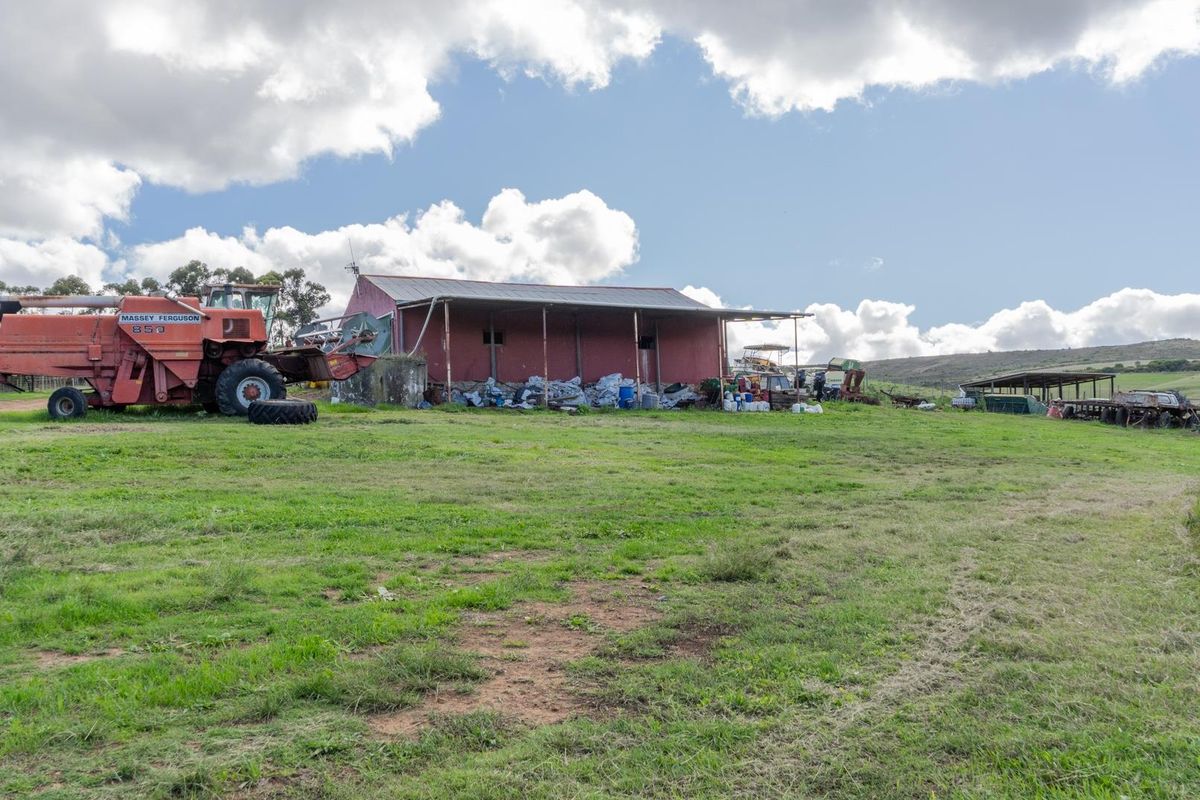 A rural farm property featuring a large red barn structure with an attached lean-to, set within an expansive open pasture landscape.