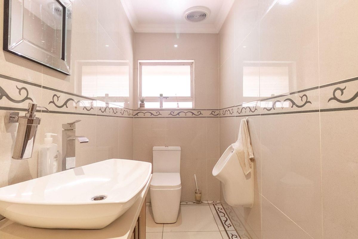 A modern bathroom featuring a vessel sink, wall-mounted toilet, and a wall-mounted urinal, finished with neutral ceramic wall and floor tiles.
