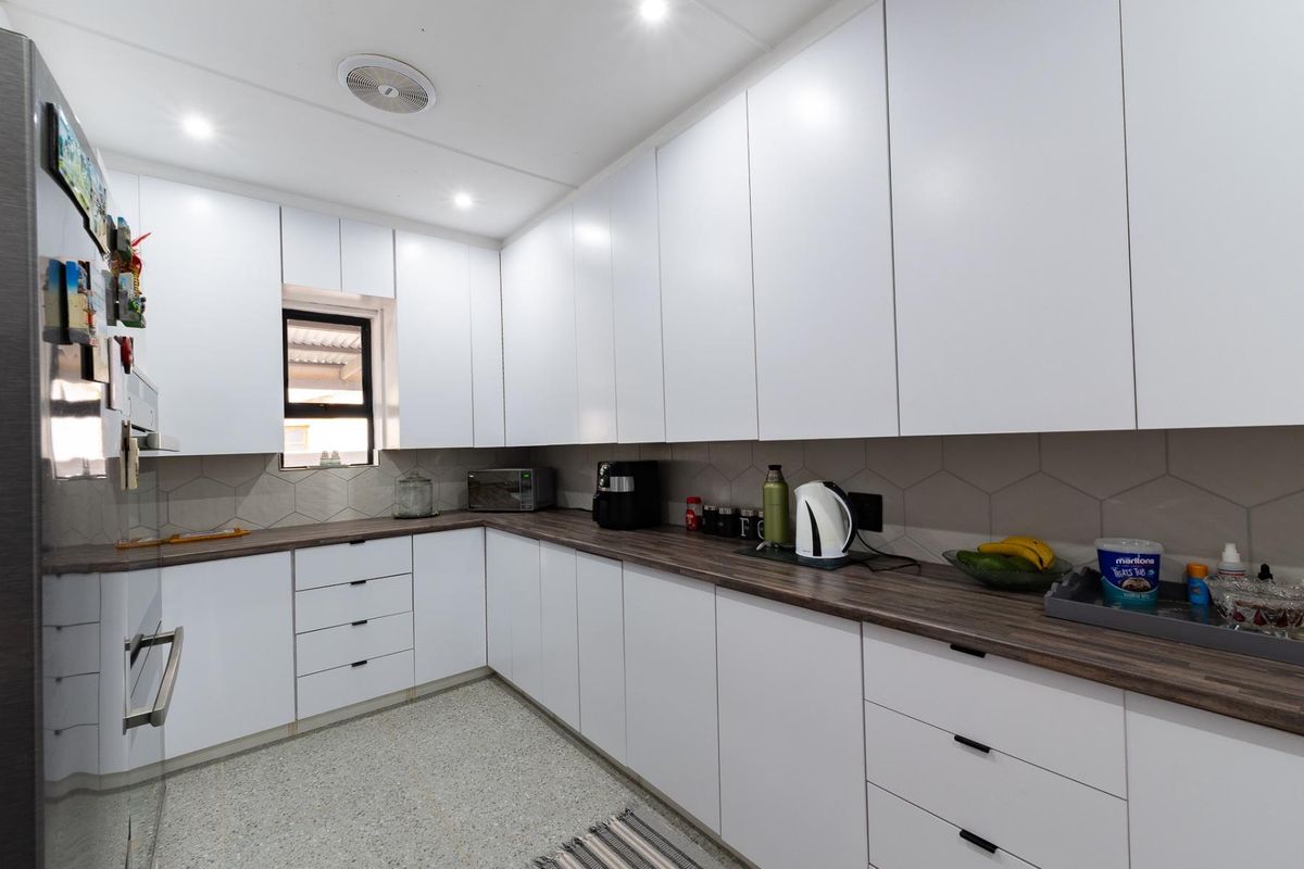 Modern kitchen featuring white handleless cabinetry, dark wood-look laminate countertops, hexagonal tile backsplash, and recessed ceiling lighting.