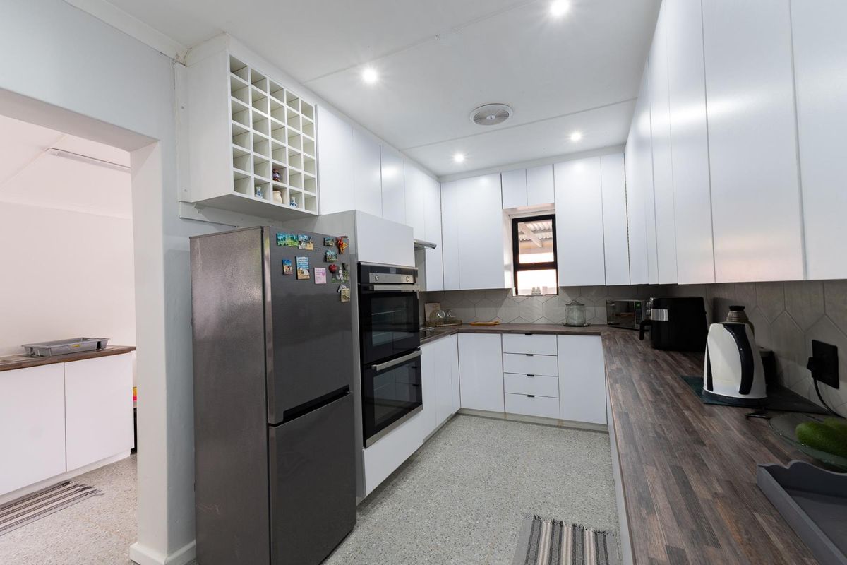 Modern kitchen featuring white cabinetry, dark wood-look countertops, built-in double oven, and tiled backsplash with recessed ceiling lighting.