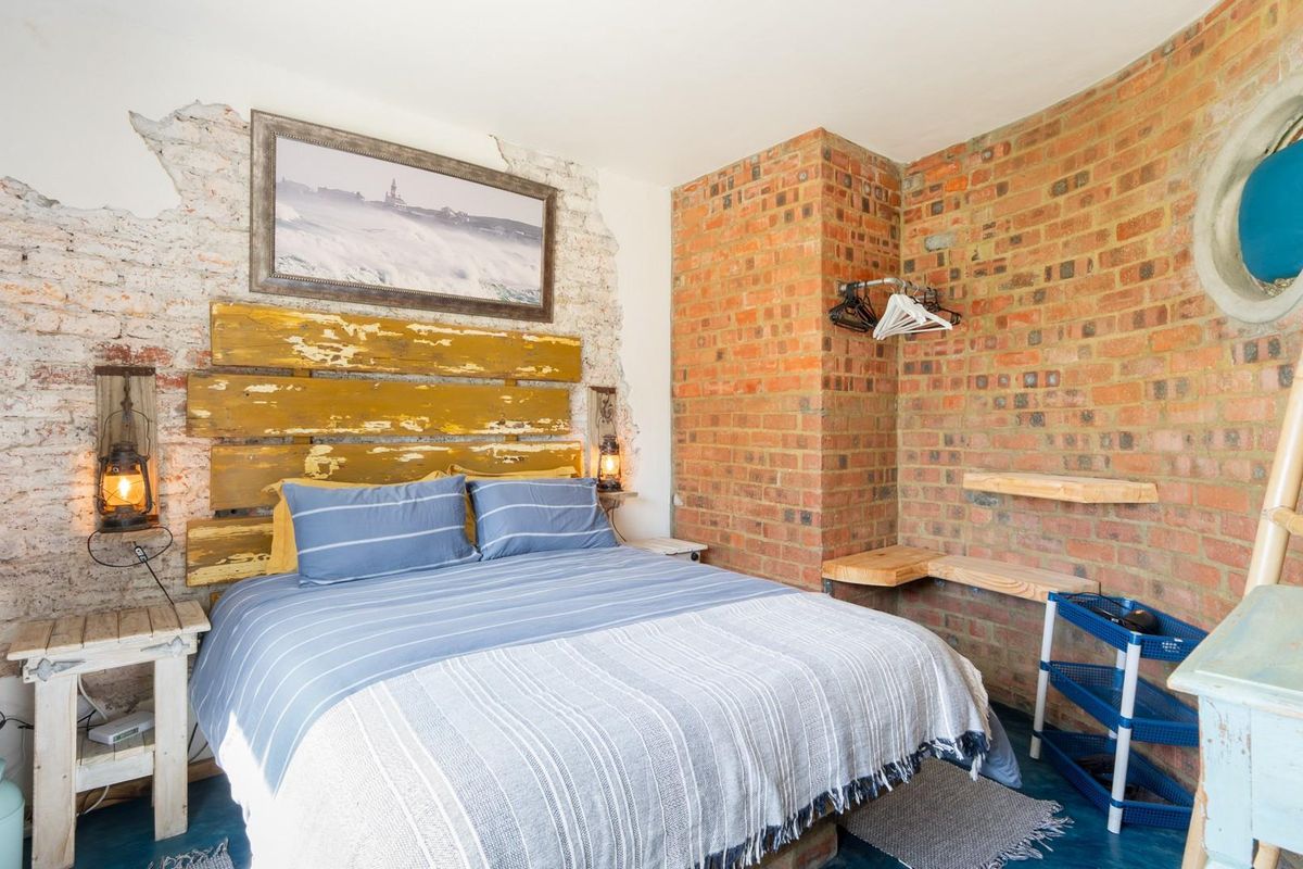 A rustic bedroom featuring exposed brick walls, a unique circular window, and built-in wooden shelving, offering a characterful and industrial-inspired living space.