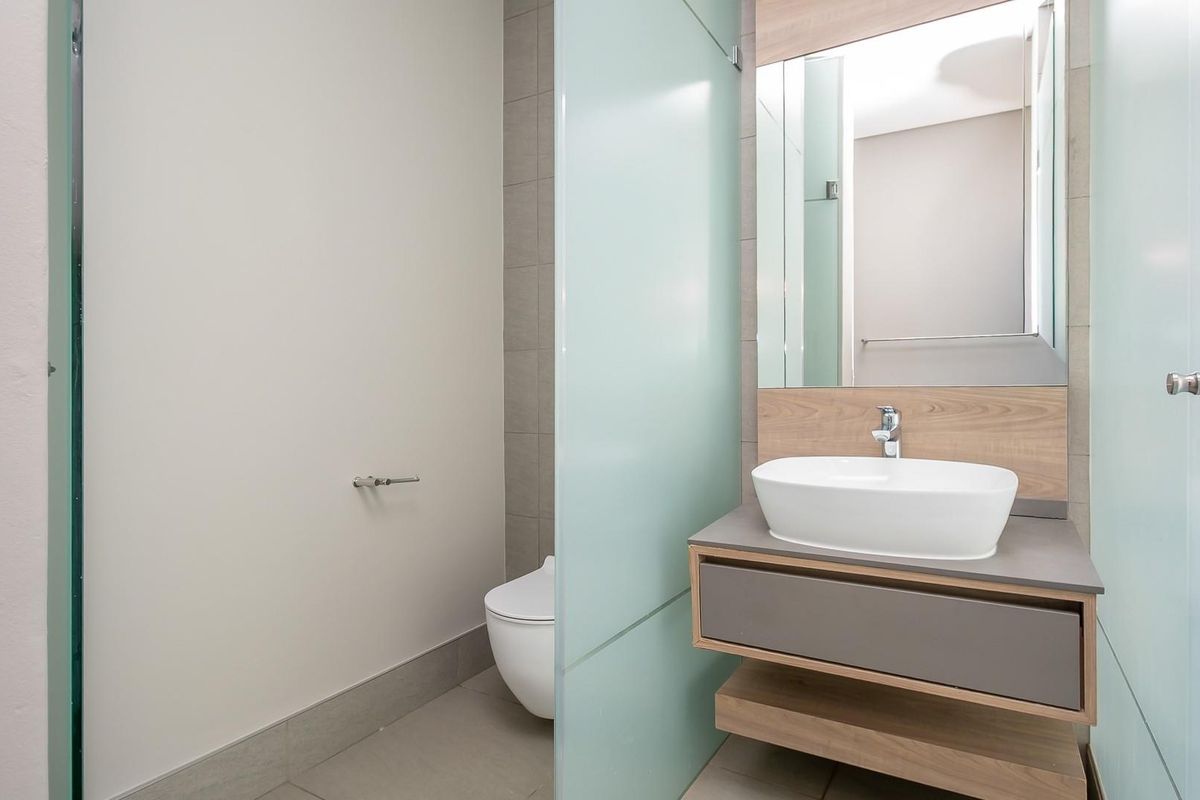 Modern bathroom featuring a floating vanity with a vessel sink, wall-mounted toilet, and frosted glass privacy screen.