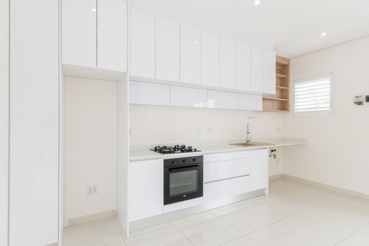 Modern kitchen featuring white high-gloss cabinetry, stone countertops, a built-in gas hob, oven, and integrated sink with tiled flooring.