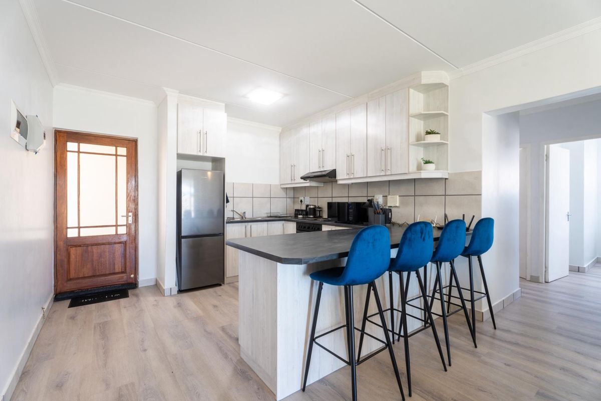 A modern kitchen featuring light wood-grain cabinetry, dark laminate countertops, a breakfast bar, and tiled backsplash, seamlessly integrated with the living area.