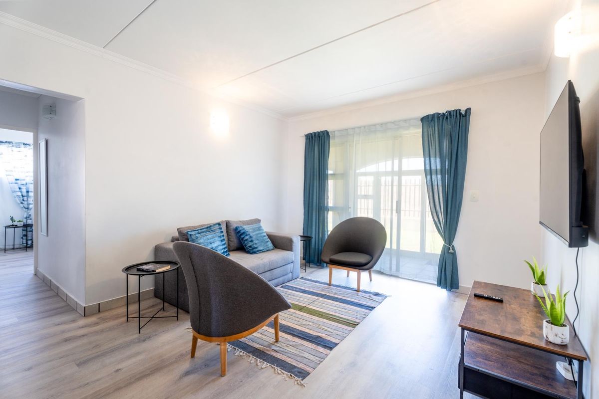 A bright and well-maintained living room featuring light-toned laminate flooring and a large sliding glass door providing access to the exterior.