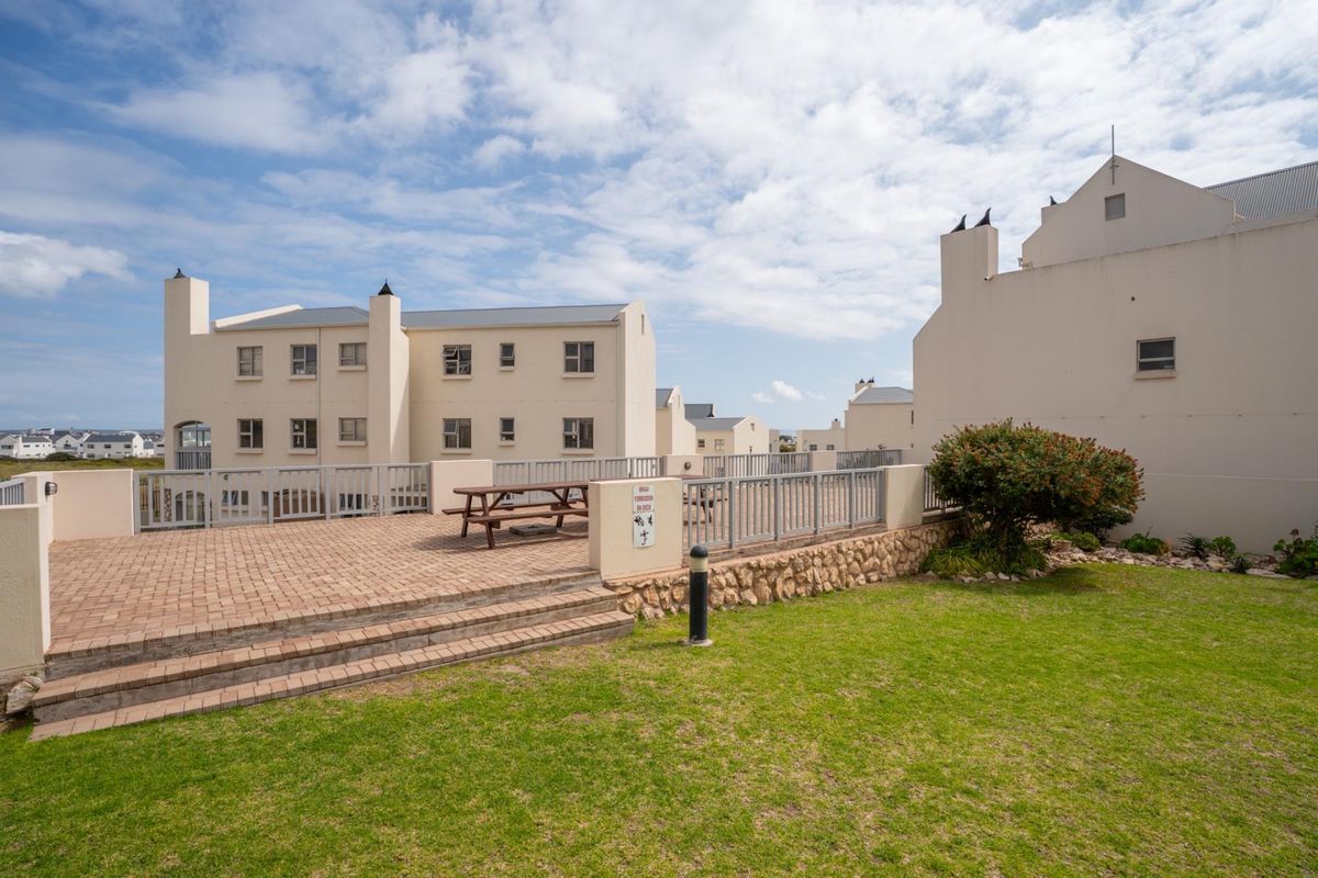 A well-maintained communal paved patio area with metal railings, stone retaining wall, and surrounding lawn within an apartment complex.