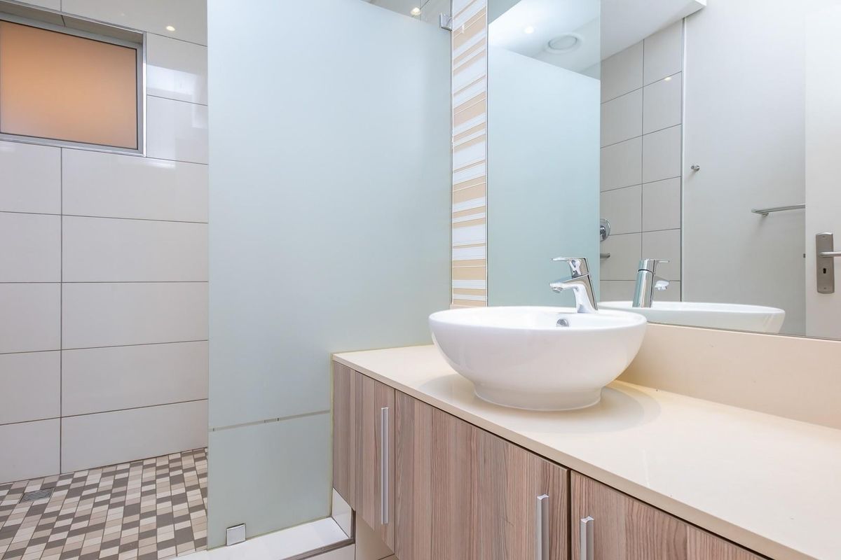 Modern bathroom featuring a vessel sink vanity, large wall mirror, and a walk-in shower with frosted glass partition and mosaic floor tiling.