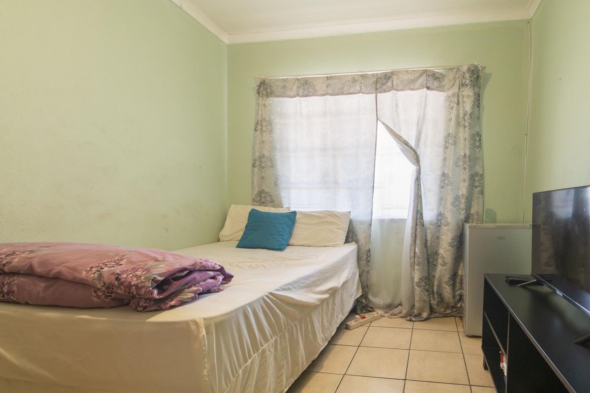 A compact bedroom featuring tiled flooring and a window with curtain fixtures.
