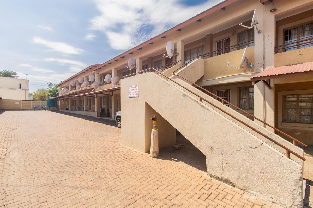 Exterior view of a multi-story apartment complex featuring a paved courtyard, external concrete staircases, and multiple satellite dishes mounted on the building facade.