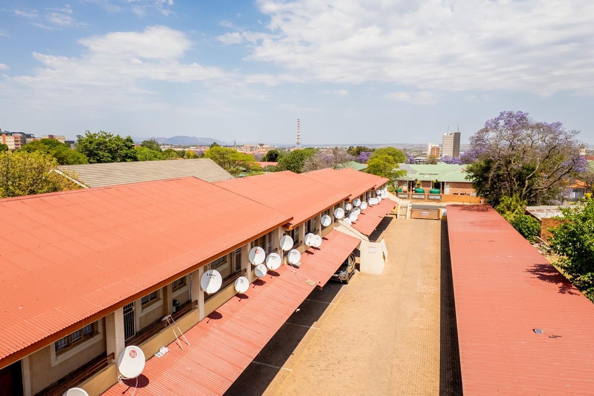 Aerial view of an apartment complex featuring long covered walkways, multiple satellite dish installations, and paved outdoor common areas.