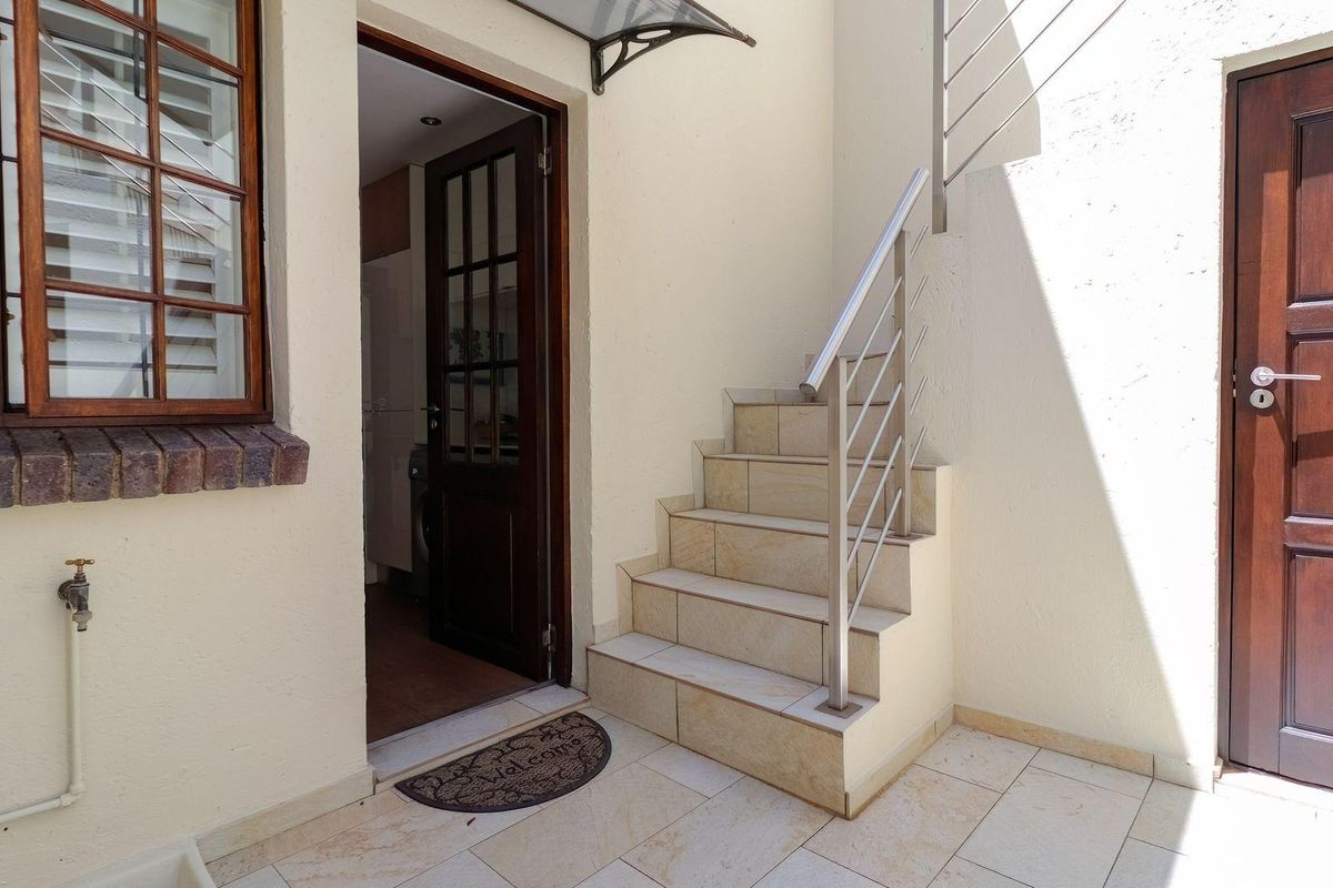 A tidy rear courtyard area featuring a tiled staircase with a stainless steel handrail, timber door access, and an external water tap.