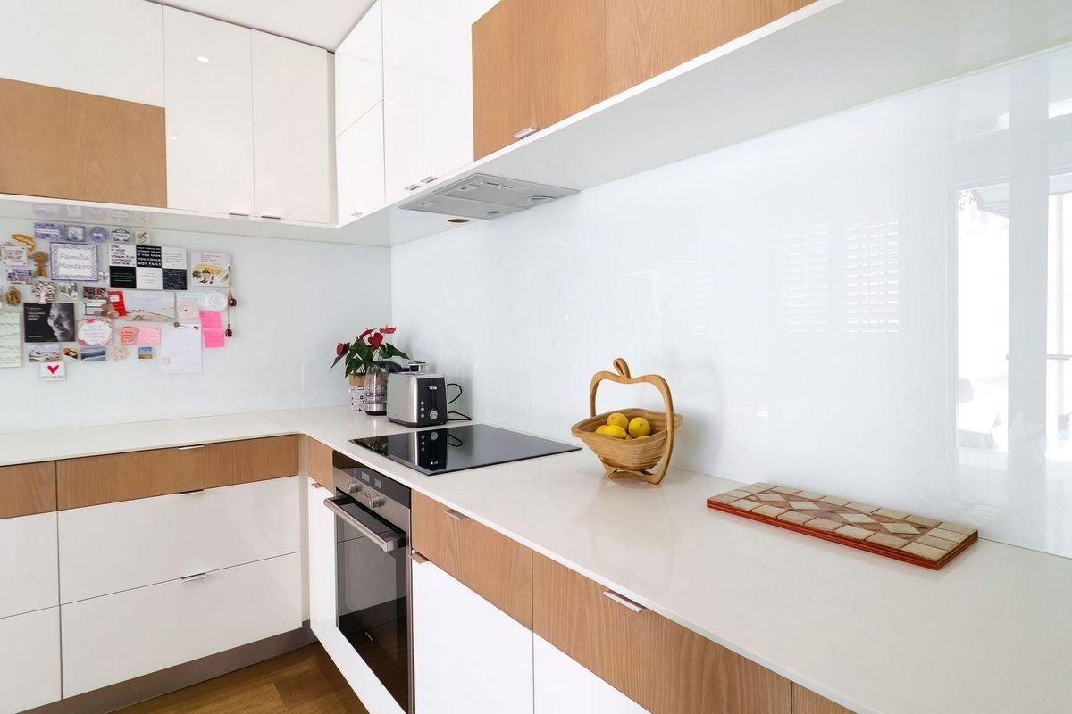 Modern kitchen featuring sleek white and wood-tone cabinetry, stone countertops, integrated appliances, and a clean glass splashback.