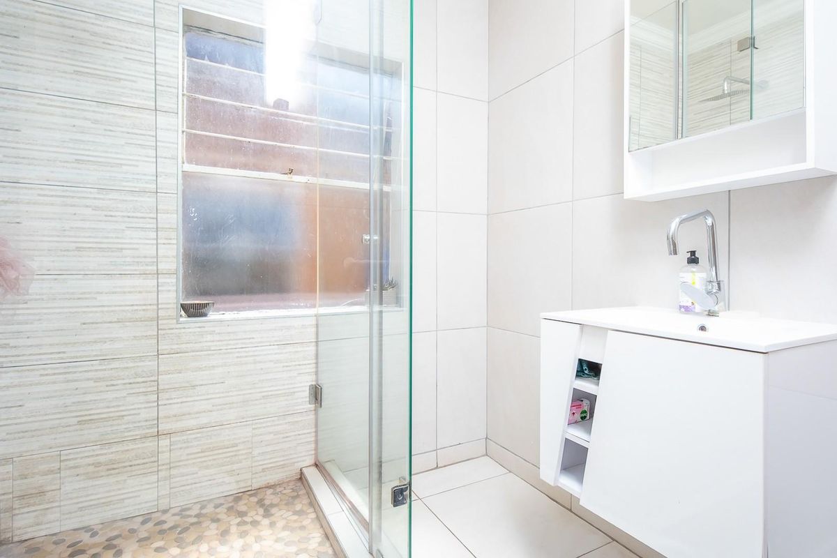 Modern bathroom featuring a glass-enclosed shower with pebble-style flooring, wall-mounted vanity with integrated basin, and neutral tiled walls.