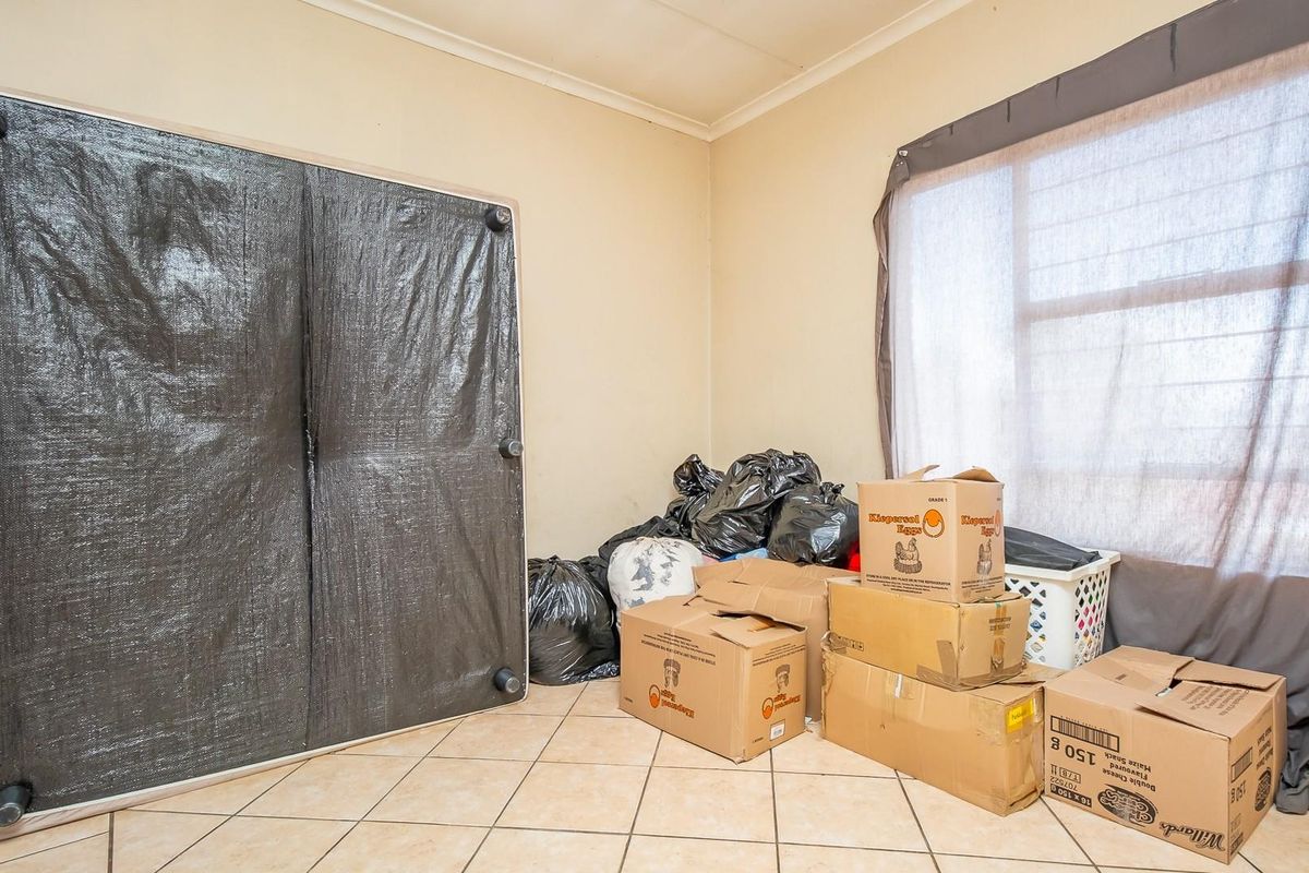 A bedroom space featuring tiled flooring and a window with curtaining, currently used for storage.