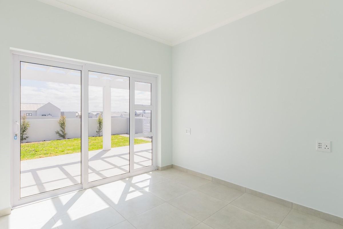 A bright, empty room featuring large sliding glass doors that open onto a paved patio and garden area.