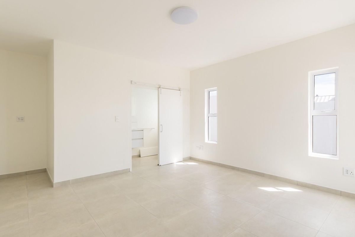 A bright, empty bedroom featuring neutral tiled flooring, white walls, and a modern sliding barn-style door leading to an adjoining space.