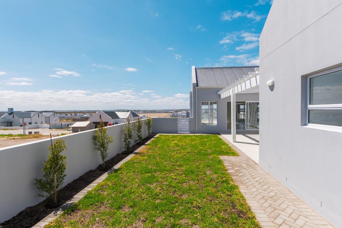 A well-maintained rear garden featuring a paved walkway, a covered patio area with a pergola, and a perimeter boundary wall.