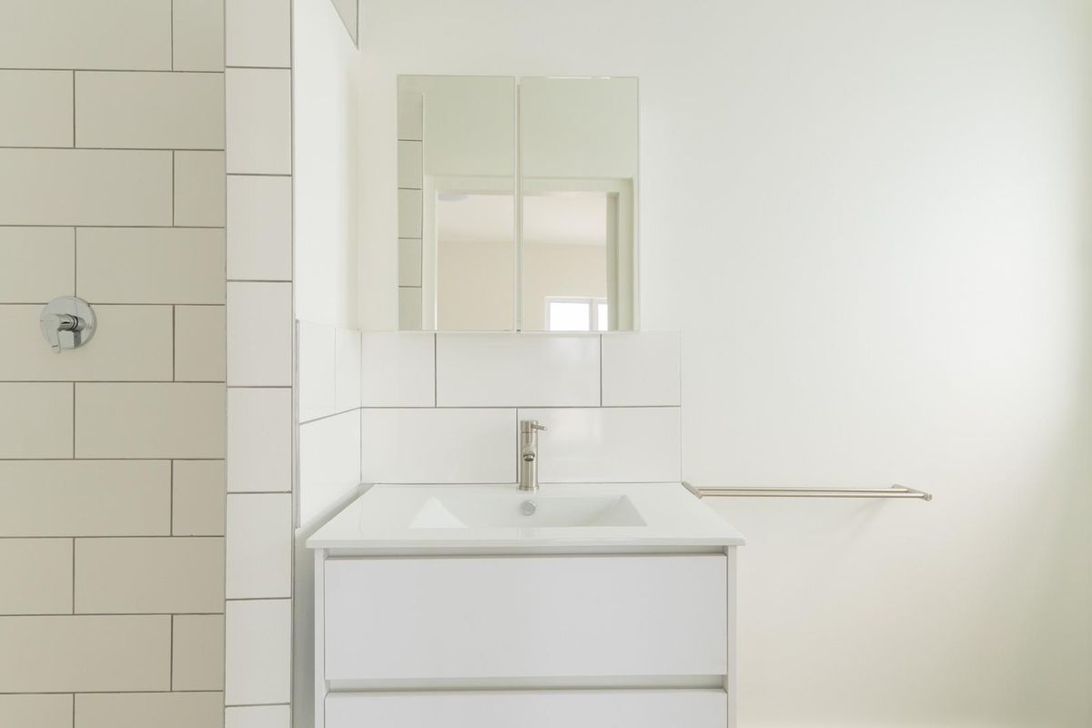 A clean, modern bathroom featuring a white vanity with integrated sink, subway tile shower surround, and a mirrored medicine cabinet.