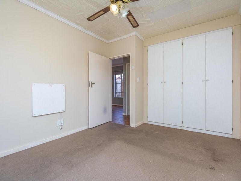 A bedroom featuring built-in cupboards, a ceiling fan, and carpeted flooring, with an adjacent hallway view.