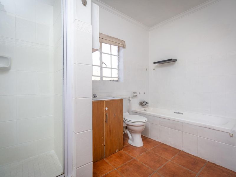 A functional bathroom featuring a separate shower, bathtub, toilet, and a vanity cabinet with a window providing natural light.