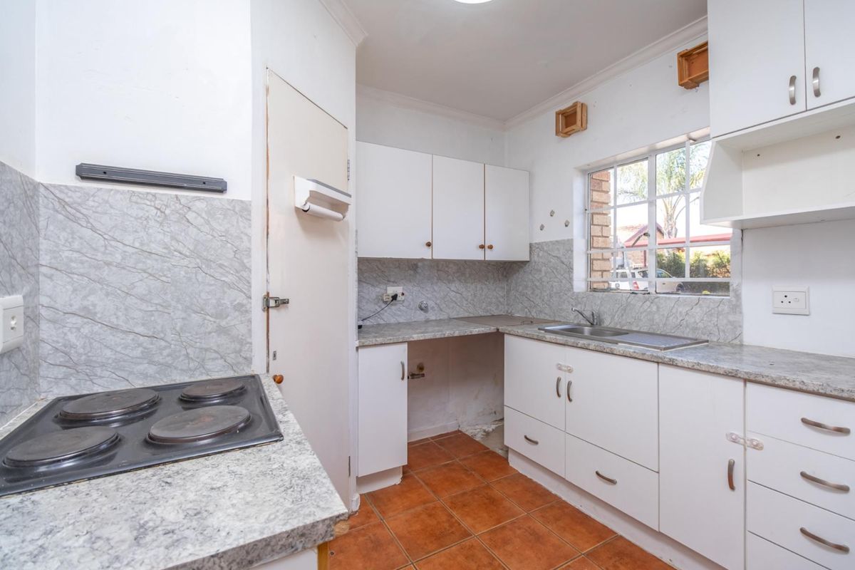 A functional kitchen featuring white cabinetry, laminate countertops, a built-in electric hob, and a stainless steel sink with tiled splashbacks.
