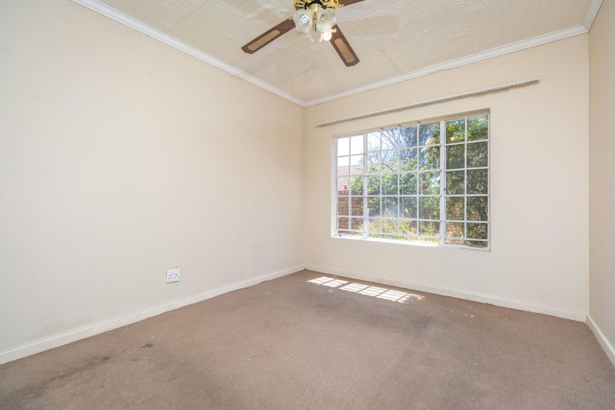 An empty bedroom featuring a ceiling fan, large window with security bars, and carpeted flooring.