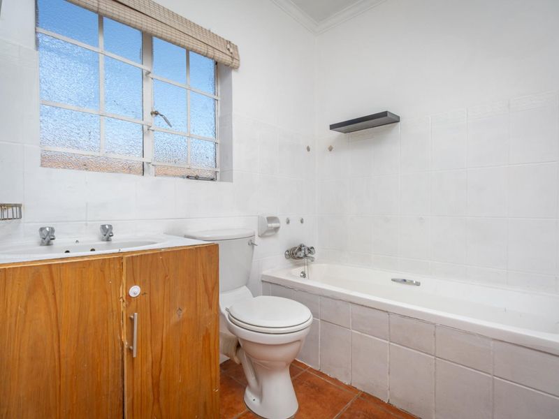 A functional bathroom featuring a built-in bathtub, vanity cabinet with integrated basin, toilet, and tiled wall finishes.