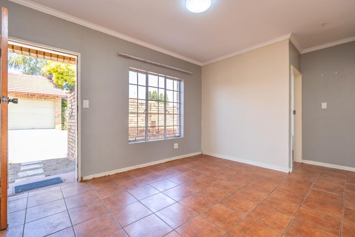 An empty living room featuring tiled flooring, a large window with security bars, and direct access to the exterior driveway area.