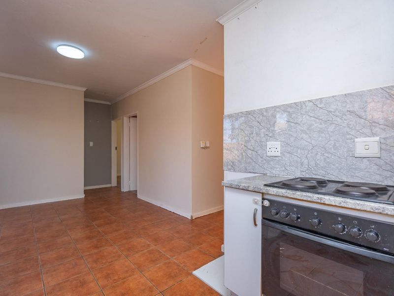 A functional kitchen area featuring a built-in oven, electric hob, and granite countertops, with tiled flooring and neutral wall finishes.