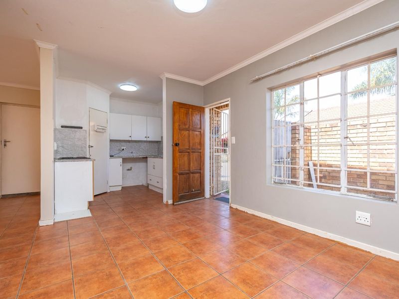 An open-plan living and kitchen area featuring tiled flooring, built-in cabinetry, and direct access to the exterior through a security-fitted timber door.