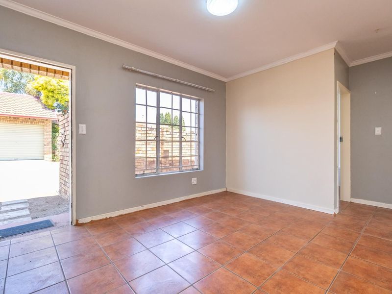 An empty living room featuring tiled flooring, neutral wall tones, and a steel-framed window with direct access to the exterior.