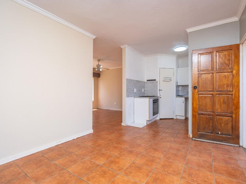 Open plan living and kitchen area featuring tiled flooring, built-in oven and stove, and a solid timber door, offering a functional blank canvas.