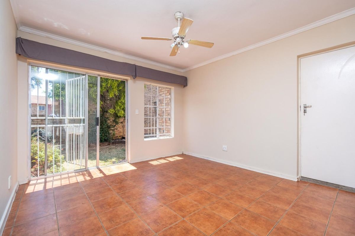 An empty living room featuring tiled flooring, a ceiling fan, and a sliding glass door providing access to the rear garden area.