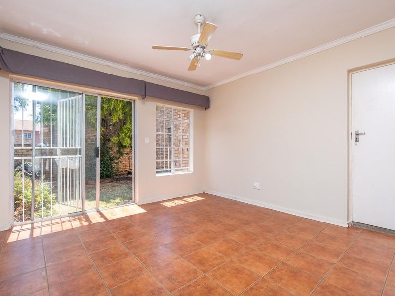 An empty living room featuring tiled flooring, a ceiling fan, and a sliding glass door providing access to the rear garden area.