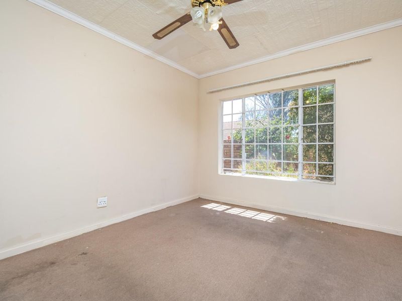 An empty bedroom featuring a ceiling fan, textured ceiling, and a large grid-pattern window overlooking the garden.