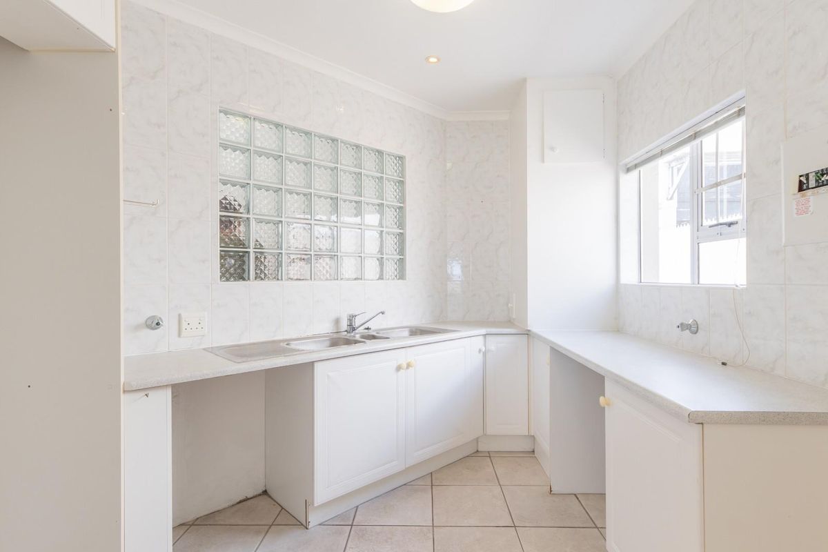 A functional kitchen featuring white cabinetry, tiled splashbacks, a double sink, and a glass block feature window, providing a bright and practical workspace.