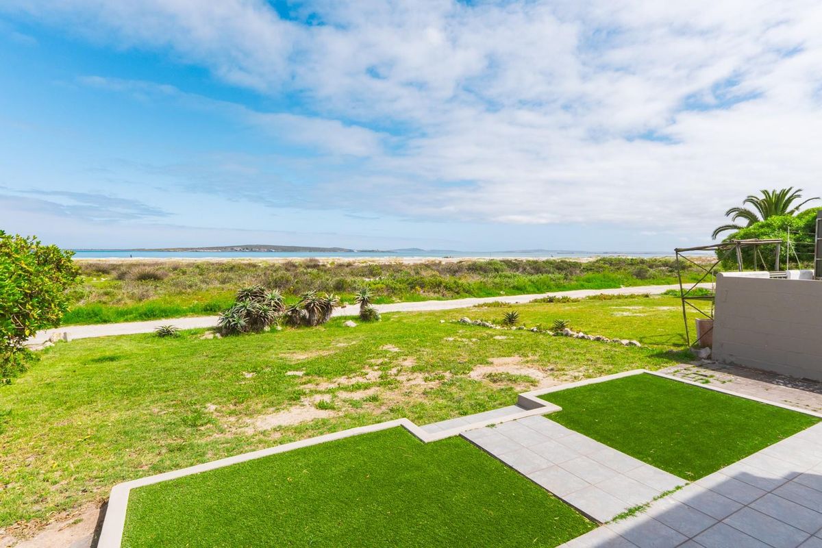 A view of the rear garden featuring a paved patio area, artificial lawn, and direct access to the coastal landscape.