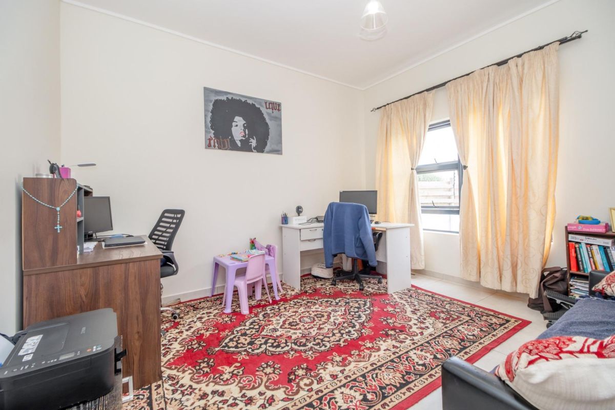 A functional bedroom currently utilized as a home office, featuring tiled flooring and a window with curtain tracks.