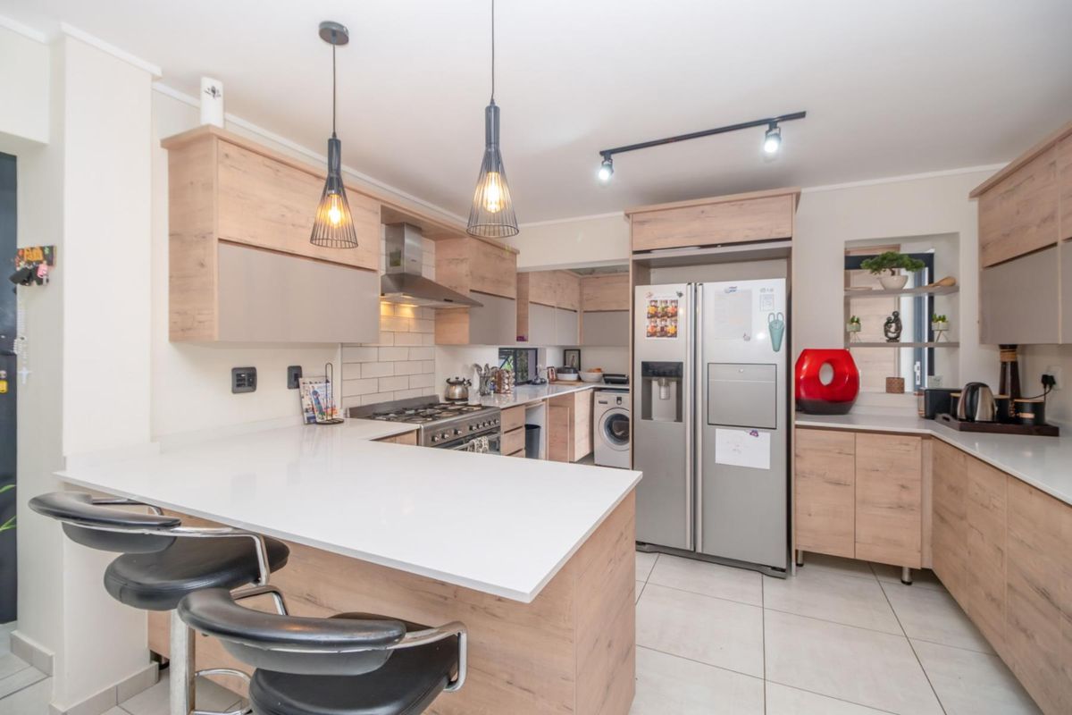 Modern kitchen featuring light wood cabinetry, stone countertops, a breakfast bar, integrated gas stove, extractor fan, and tiled flooring.