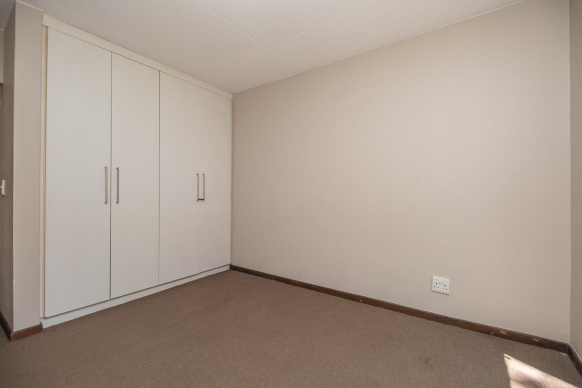 A clean, empty bedroom featuring neutral wall tones, fitted built-in wardrobes, and carpeted flooring, offering a versatile space ready for personalization.