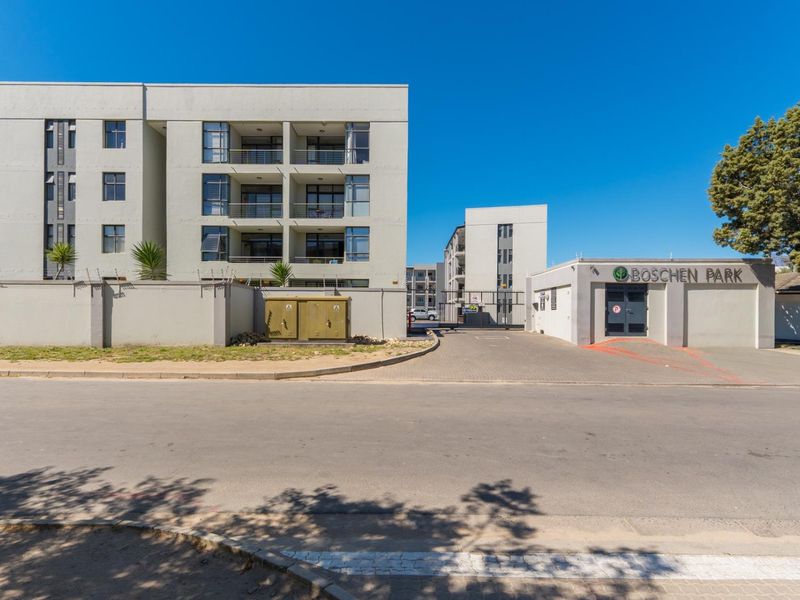 Street view of the Boschen Park apartment complex entrance, featuring a paved driveway, secure gated access, and modern multi-story residential building facades.