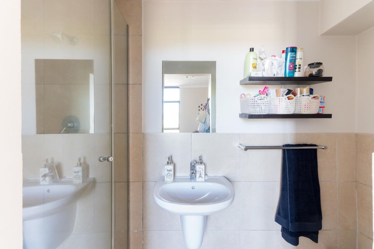 A functional bathroom featuring a pedestal basin, mixer tap, and a glass-enclosed shower with neutral wall tiling.