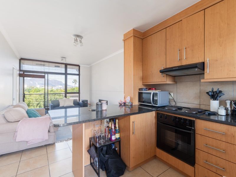 Open-plan kitchen and living area featuring wooden cabinetry, granite countertops, built-in appliances, and direct access to a balcony with scenic views.