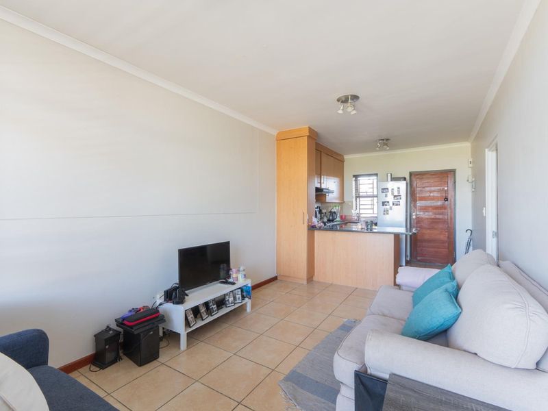 Open-plan living area featuring tiled flooring and a functional kitchen with built-in cabinetry and counter space, leading to the main entrance.