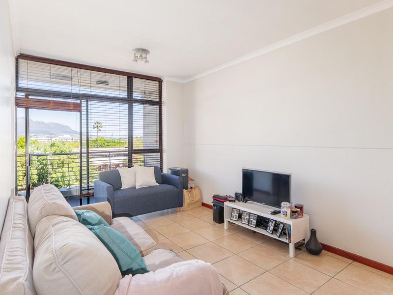 A bright living room featuring tiled flooring, a large sliding glass door with balcony access, and venetian blinds, offering natural light and mountain views.